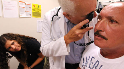 Leonard Zadecky looks at blood vessels in patient Joe Lema's eye as intern Cara Moses observes at the Community Health Clinic of Butler County.