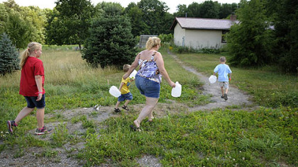 Shelley Carlson, 42, center, walks to fill up gallon water jugs behind a Lutheran church camp several miles from her home in the Woodlands in June. A family friend, Kayla Zeidler, 10, left and two of Ms. Carlson's three sons, Dylan, 3, and Logan, 6, race to help her.  Ms. Carlson noticed an odor and discoloration in her tap water in January 2011.