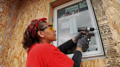 Nakeia Dismond, an Eco-Village home owner, helps install the first window in her River Falls, Wis., home.The energy-saving window is one of many energy-efficient features used in Eco-Village, a Habitat for Humanity project.