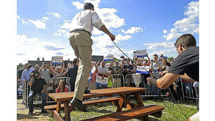 An overflow crowd cheers as Republican presidential nominee Mitt Romney gets on a table to speak Monday as he campaigns at PR Machine Works in Ontario, Ohio.