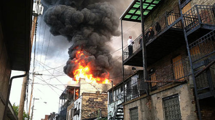Flames continued to shoot from a building along Merchant Street in Ambridge that caught fire before dawn Friday.
