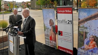 Jared Cohon, president of Carnegie Mellon University, stands near as Henry Hillman speaks  about CMU's first-of-its-kind traffic signal control system. A pilot project for the synchronized signals reduced vehicle wait time in the high-traffic sections of East Liberty by 40 percent. The event was held in front of the Target store near Penn Avenue and Penn Circle.
