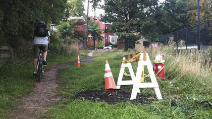 A cyclist rides past the sinkhole after Pittsburgh's public works crews filled it in with recycled asphalt and marked it with a sawhorse.