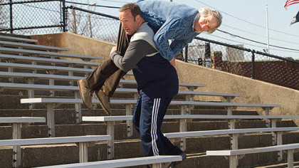 As Scott Voss, Kevin James carries Henry Winkler, who portrays a fellow teacher, over his shoulder as added weight while he works out for mixed martial arts fighting in "Here Comes the Boom."