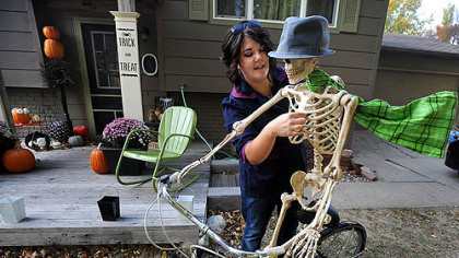 Paige Kaske threads a wire through the ribcage of a skeleton to create the effect of a scarf blowing while decorating her yard this week for Halloween in Sioux Falls, S.D.