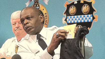 Pittsburgh Police Chief Nate Harper holds up the bullet-resistant vest worn by Officer Andrew Baker, right, to show the bullet hole in the center-chest area.
