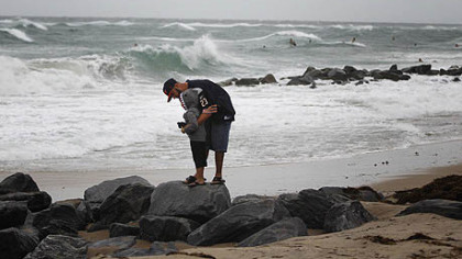 A man and his son watch the rough surf at the inlet in Boynton Beach, Fla., from Hurricane Sandy. Even if the storm doesn't come to Pittsburgh, the weather here will still take a downturn this weekend.
