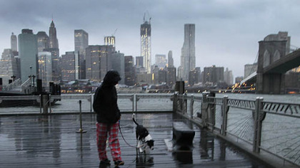 Vanessa Pumo walks her dog Bella as wind and rain from Hurricane Sandy arrive, Monday, Oct. 29, 2012 in Brooklyn, N.Y. Behind her is the Manhattan skyline and Brooklyn Bridge, right.