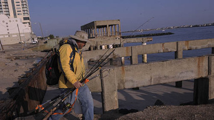 Ray Guangon, of Cherry Hill, N.J., crosses over the remains of the boardwalk north of the casino district in Atlantic City to go fishing on Saturday. The boardwalk in front of the casinos remained intact. Only an older section of the boardwalk north of the Revel casino was demolished.