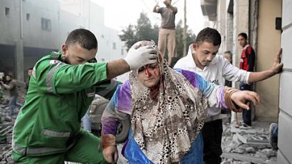 A Palestinian woman is helped by a paramedic Monday from her Gaza City residence, damaged during an Israeli air raid.