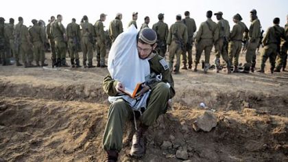 An Israeli soldier holds Torah scrolls as prays Monday at an Israeli army deployment area near the Israel-Gaza Strip border in preparation for a potential ground operation in the Palestinian coastal enclave.