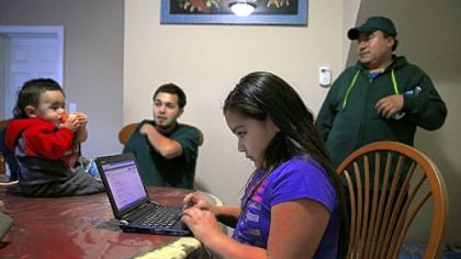 Leslie Mendoza uses a laptop as her father, Felipe, right, his nephew Aaron Carillo and Carillo's son, Jayden, talk in the home they rent in Aurora, Ill.
