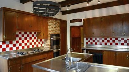 The kitchen has stainless-steel countertops and a built-in stovetop and oven. Wood beams and brickwork surround the two ovens.
