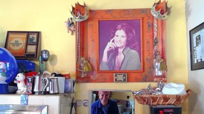 Older Carman looks out from her little kitchen under the gaze of younger Carman.