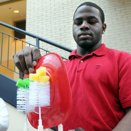 Carnegie Mellon University senior Ben Antoine demonstrates his team's scrub master with rotating brushes to clean dinnerware when placed in a sink.