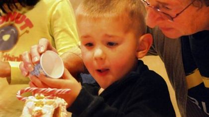 Hayden Hauck, 3, gets help from his grandmother, Linda Hauck, as he adds "snow" to his gingerbread house.