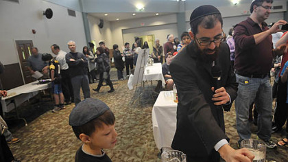 Joshua Sakolsky, 7, who won the honor of helping to fill in the first letter of Beth El Synagogue's new "inclusionary Torah,"  watches as scribe Rabbi Levi Selwyn explains how he washes his hands and says the proper proper blessing before beginning to work on the new Torah scroll. Joshua and the members of his family who helped hold the quill used to write the first letter also washed their hands and said the blessing.