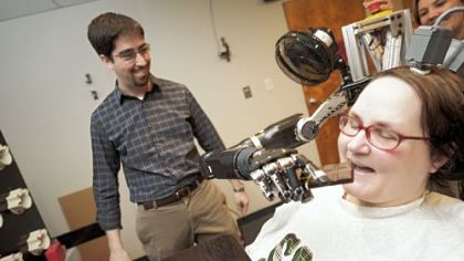 Jan Scheuermann, who has quadriplegia, takes a bite from a chocolate bar she has guided into her mouth with a thought-controlled robot arm. Research assistants Brian Wodlinger and Dr. Elke Brown watch.