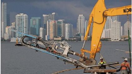 The Miami skyline frames construction crews and equipment at work on the 7-foot wharf expansion necessitated by the deepening of the Panama Canal.