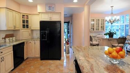 The kitchen features two islands with granite countertops, custom cabinetry and a ceramic tile floor. One of the islands overlooks the back patio through large corner windows and has a built-in pantry.