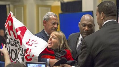 A protester who displayed a sign and briefly delayed the NRA news conference Friday in Washington is removed from the room. The United States' most powerful pro-gun lobbying group, the National Rifle Association, called Friday for armed police or security guards to be deployed to every school in the country.