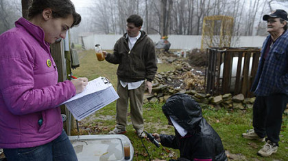 Renee Krynock, 22, of Apollo, left, and Shyama Alawattegama, 36, of Sri Lanka collect water samples from residents Dennis Higgins, rear, and his father-in-law Dave Romito, far right, of the Woodlands in Connoquenessing Township. Ms. Krynock and Ms. Alawattegama are graduate students at Duquesne University. They are conducting tests for water quality under the direction of professor John Stolz.