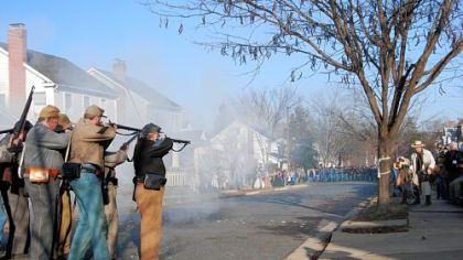 A Confederate unit fires upon advancing Union soldiers on Hanover Street in Fredericksburg, Va. A photographer in period garb, right, sets up to take a picture.